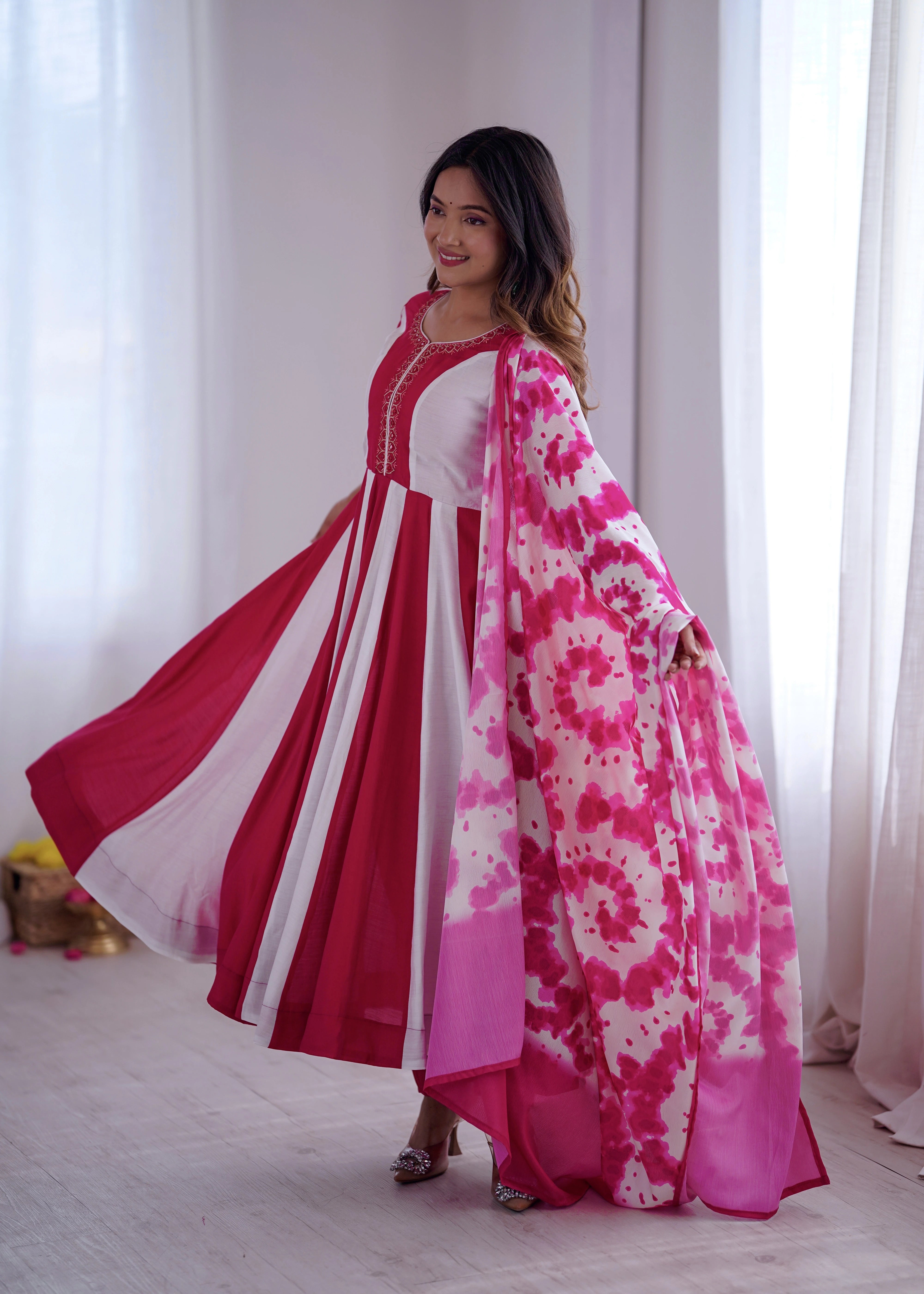 Woman wearing a red and white traditional outfit with a pink and white floral shawl in a bright room.